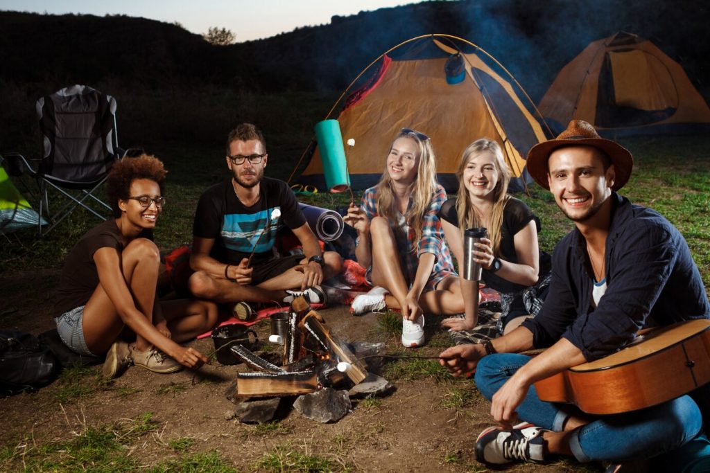 friends-sitting-near-bonfire-smiling-playing-guitar-camping-grill-marshmallow